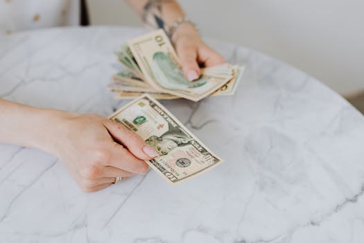 Close-up of hands counting US dollar bills on a marble table surface.